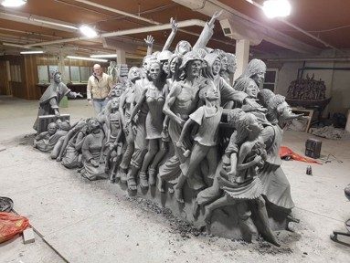 A large multi-figure sculpture with a person alongside for scale